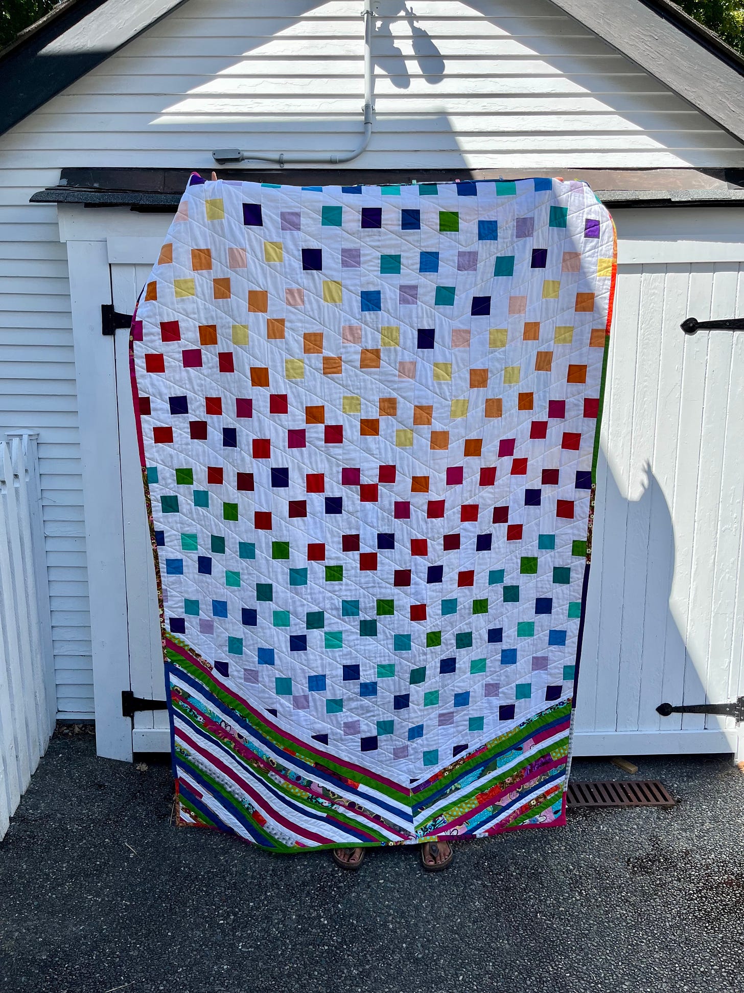 a large rainbow quilt with squares of different colors that have a waterfall type patter, a big chevron and strip pieces of fabric at the bottom that make an abstract kind of arrow effect