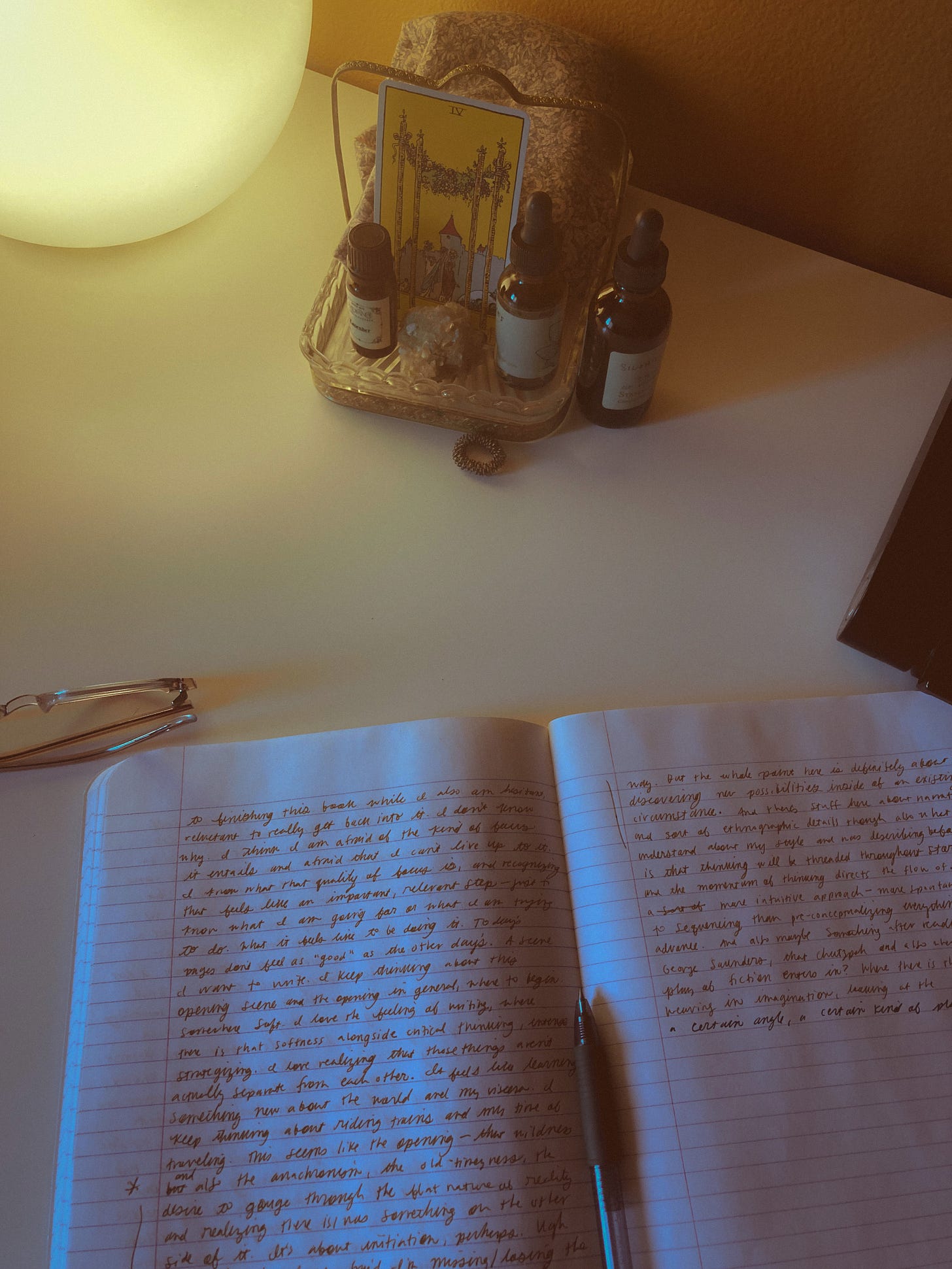 A notebook on a desk next to a lamp and tarot card deck