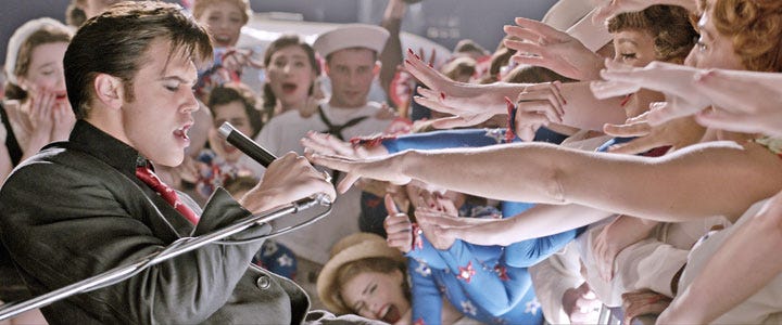 Still from Elvis (2022) of fans reaching out to try and touch a singing Elvis Presley.