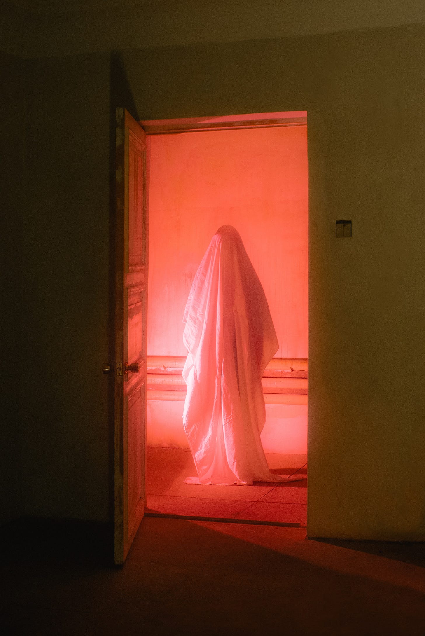 A sheet ghost floating in midair in a hallway, bathed in pink light.