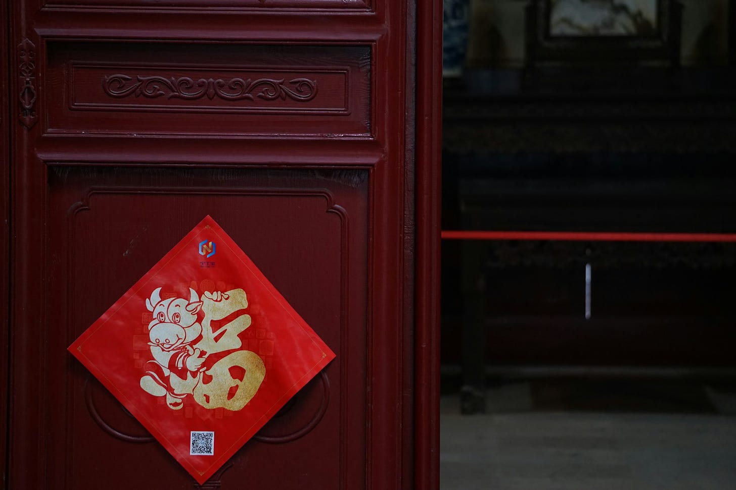 Fotografia em cores de porta de madeira com amuleto vermelho com caracter dourado para atrair boa fortuna.