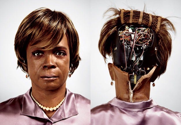 The face of a Black woman with short brownish hair; we can also see the top of a mauve silk shirt and she's wearing a pearl necklace. Alongside this image is the back of her head, open, displaying tons of wires and computery bits and bobs. The face is expressionless, hollow, and very uncanny valley.