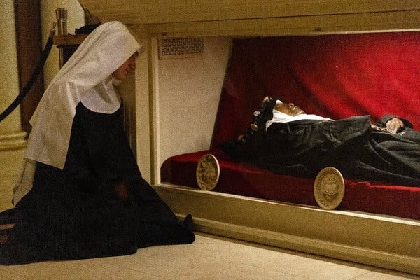 A nun kneels in front of a glass box with the body of Sister Wilhelmina.