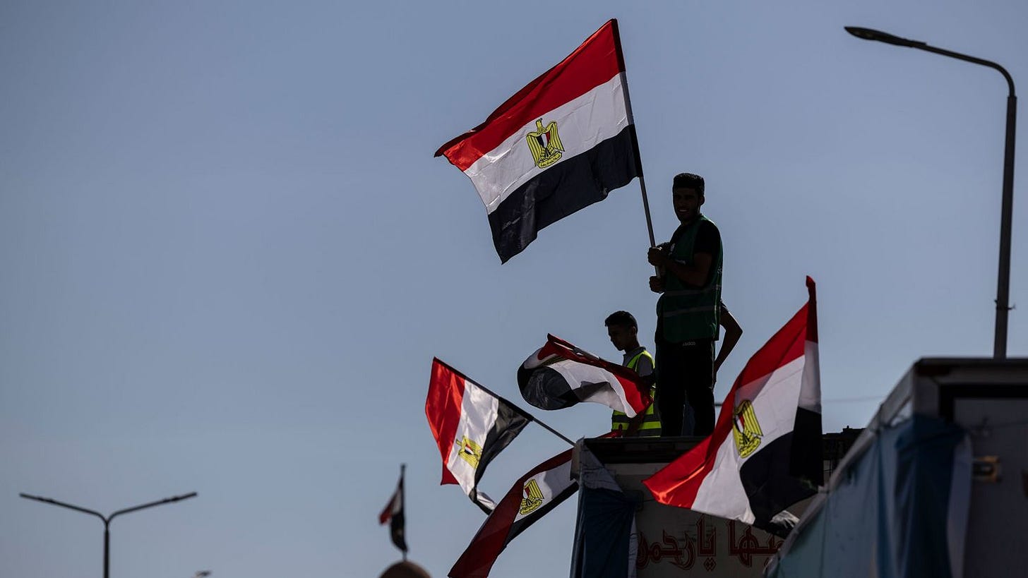 Volunteers carry Egyptian flags as they wait with aid convoy trucks loaded with supplies near the North Sinai Governorate building on October 15, 2023 in North Sinai, Egypt. 