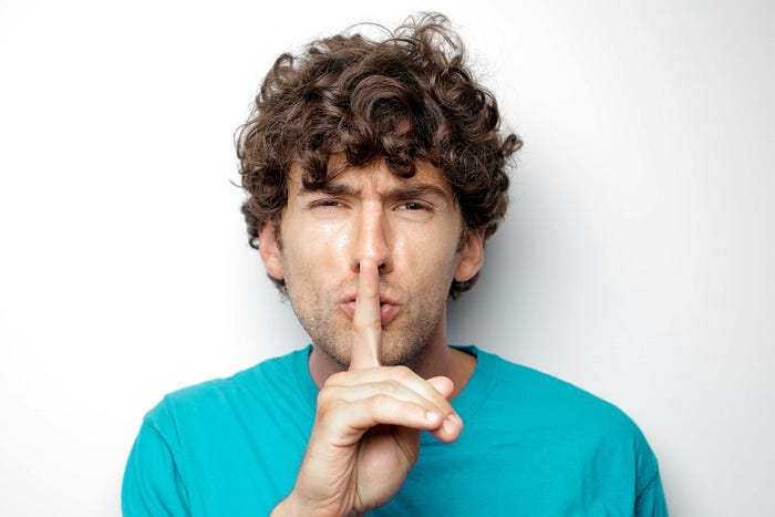 A man holding up a finger to his lips and going “shush” to quiet a person