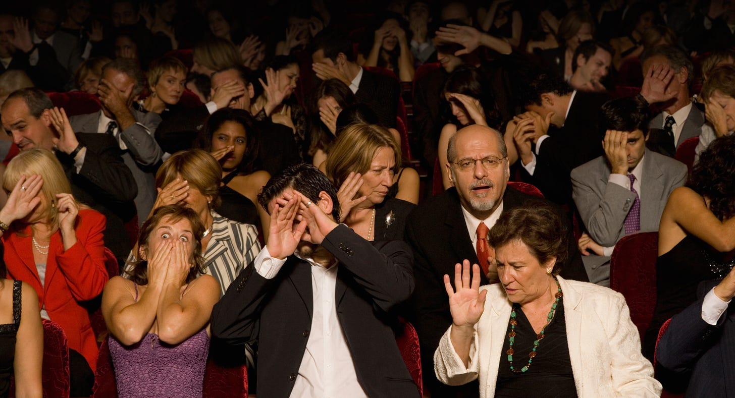 Crowd of people in audience with hands over faces or shocked expressions