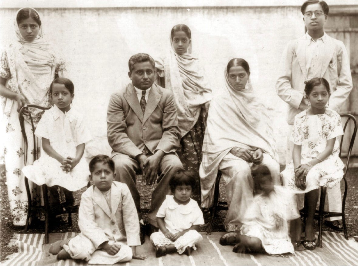 A sepia toned image featuring Qudsiya’s great grandparents, Abbas Ali and Asma, with eight of their ten children. All are in their best clothes, with neutral, almost stern expressions. Standing in the rear are the three oldest children, Salma, Bilquis, and Yusuf. The girls have their heads covered, while Yusuf wears glasses. Seated in the middle are Sofia (another daughter), Abbas Ali, Asma, and Kubra (Qudsiya’s grandmother). The girls and Asma wear white; Abbas, a perhaps tan western suit; he is clean shaven with shiny hair. Sitting on the ground are the youngest children: Mustanir, Hanifa, and Hanida.