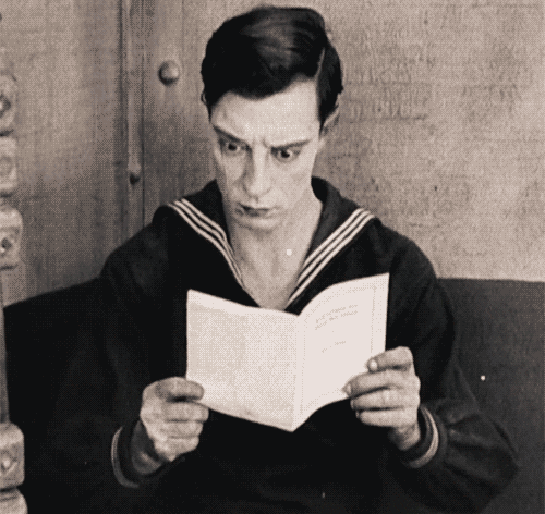 Black and white gif of Buster Keaton opening a page on a simple pamphlet repeatedly.