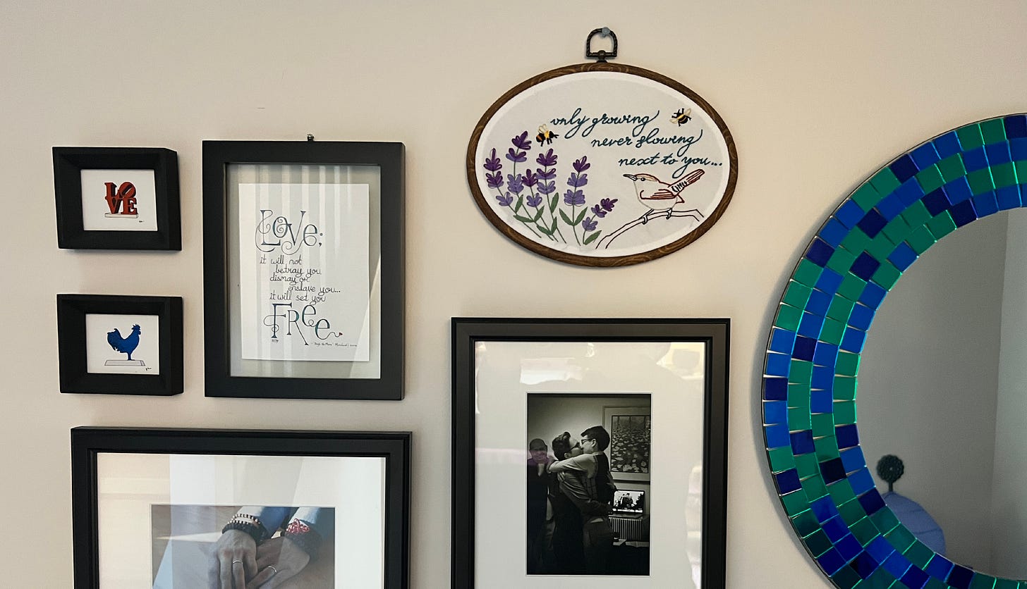 Photo of the completed embroidery piece hanging above a wedding photo and to the left of some other lyrics text artwork on a white wall. 