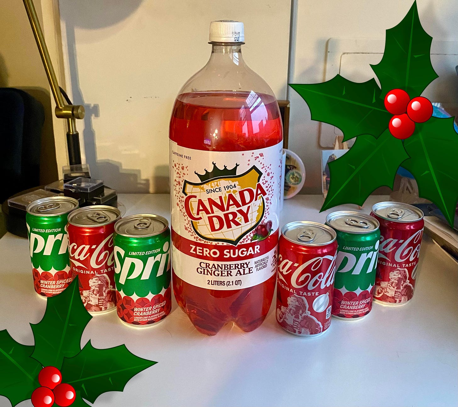 Cranberry Sprite, Cranberry Canada Dry, and cokes in Christmas cans, lined up on a desk