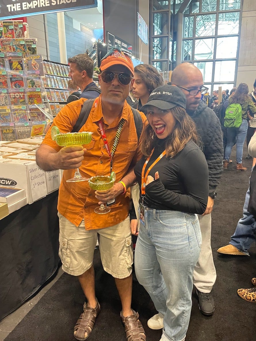 Lauren poses with a thumbs up next to a man in an orange short-sleeve button up, khaki cargo pants, orange baseball cap, tinted aviator sunglasses and two huge margaritaville glasses