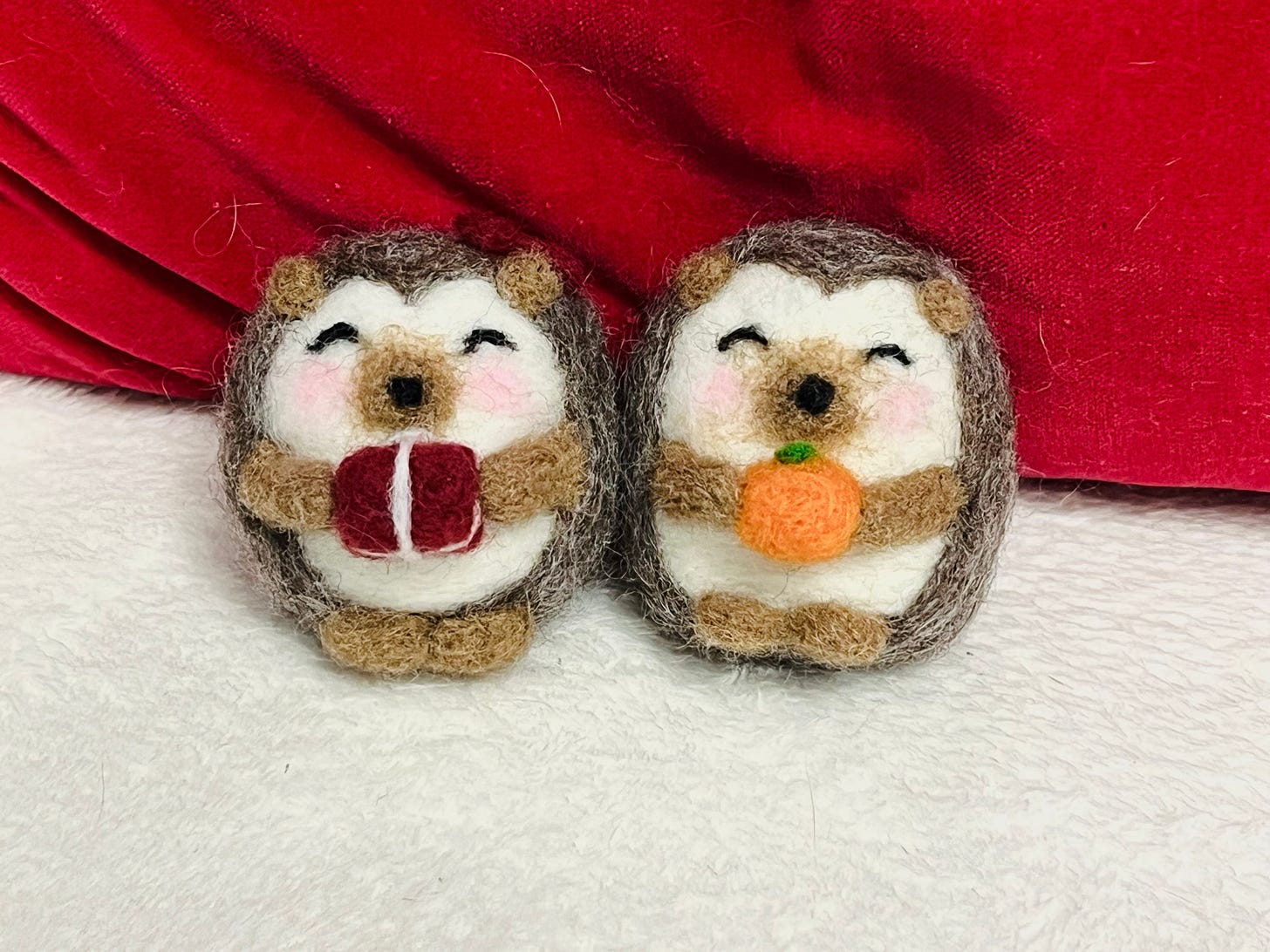 two needle-felted hedgehogs holding a red present and an orange pumpkin