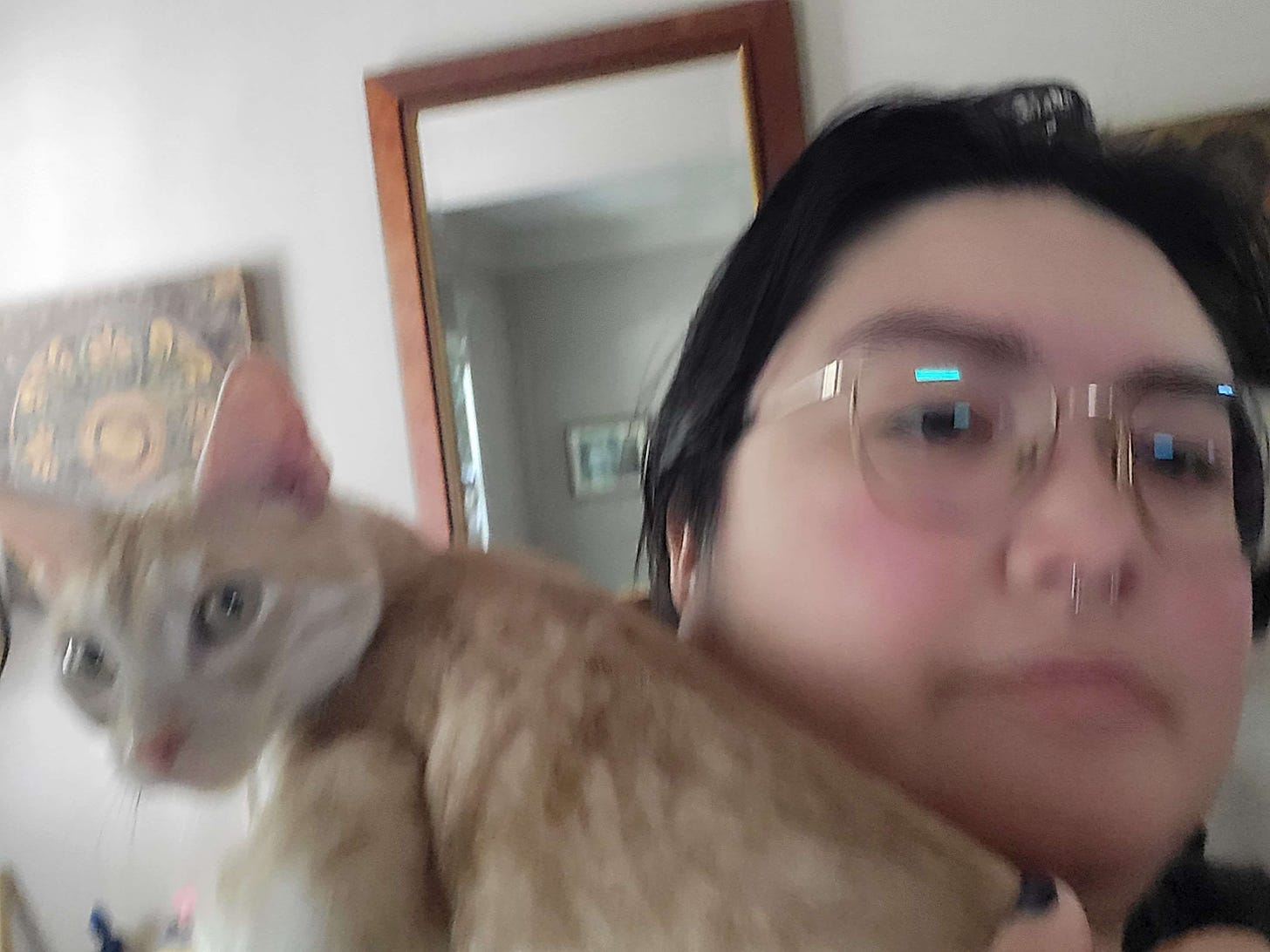 blurry selfie of me and an orange cat perched on my shoulder