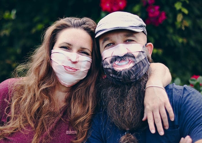 A man and a woman wearing masks that make them appear to be smiling, but their eyes convey how tired they actually are.