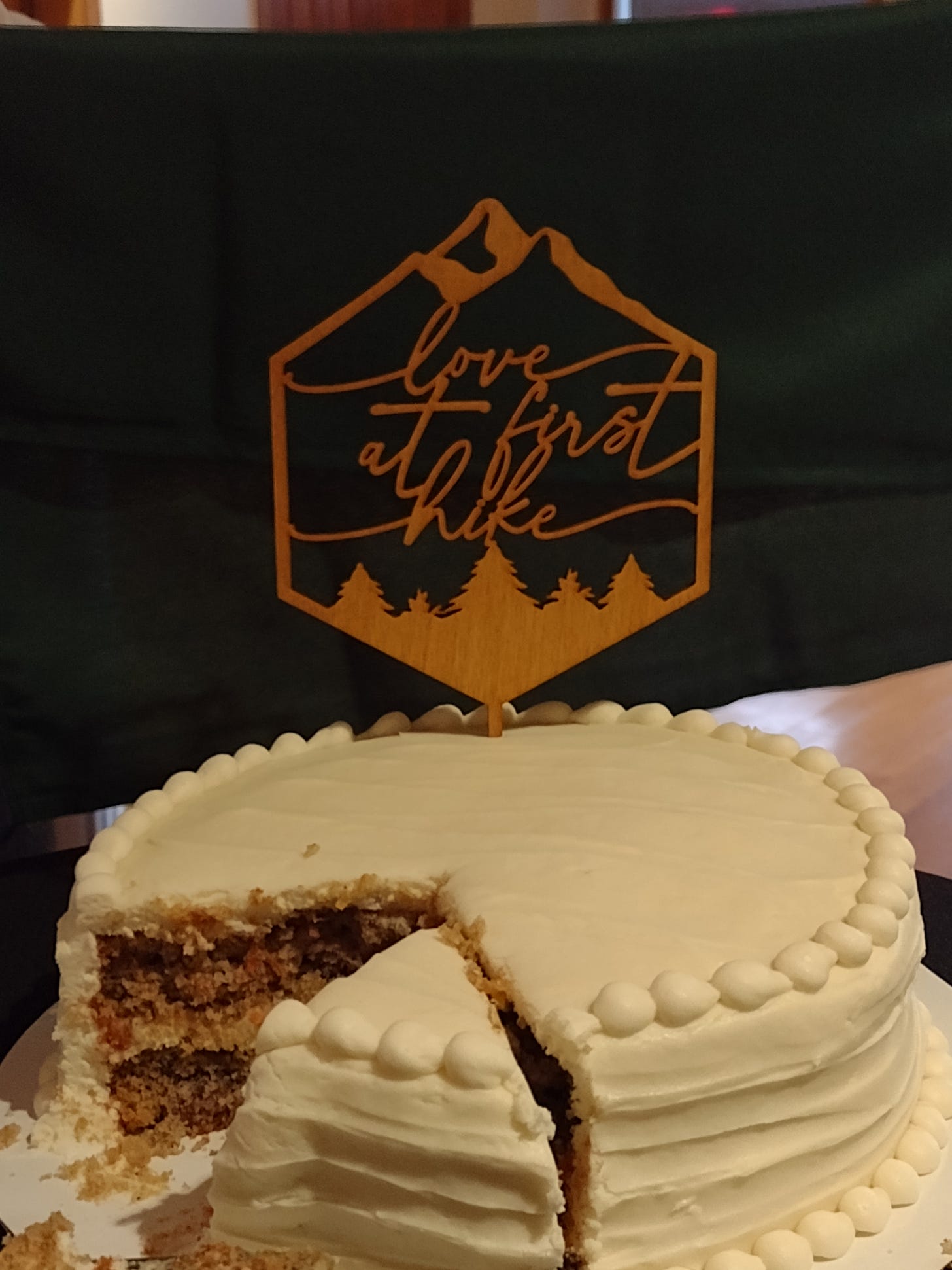 a white frosted cake with a topper that says 'love at first hike'
