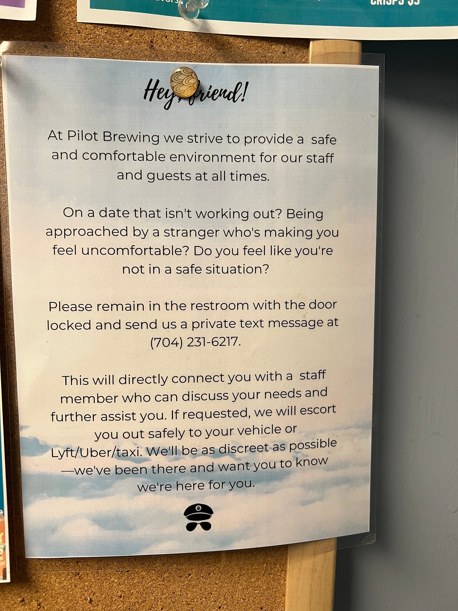 Alt Text: A sign that reads “Hey friend! At Pilot Brewing we strive to provide a safe and comfortable environment for our staff and guests at all times. On a date that isn’t working out? Being approached by a stranger who’s making you uncomfortable? Do you feel like you’re not in a safe situation? Please remain in the restroom with the door locked and send us a private text message at (704)231-6217. This will directly connect you with a staff member who can discuss your needs and further assist you. If requested, we will escort you out safely to your vehicle or Lyft/Uber/taxi. We’ll be as discreet as possible - we’ve been there and want you to know we’re here for you.”