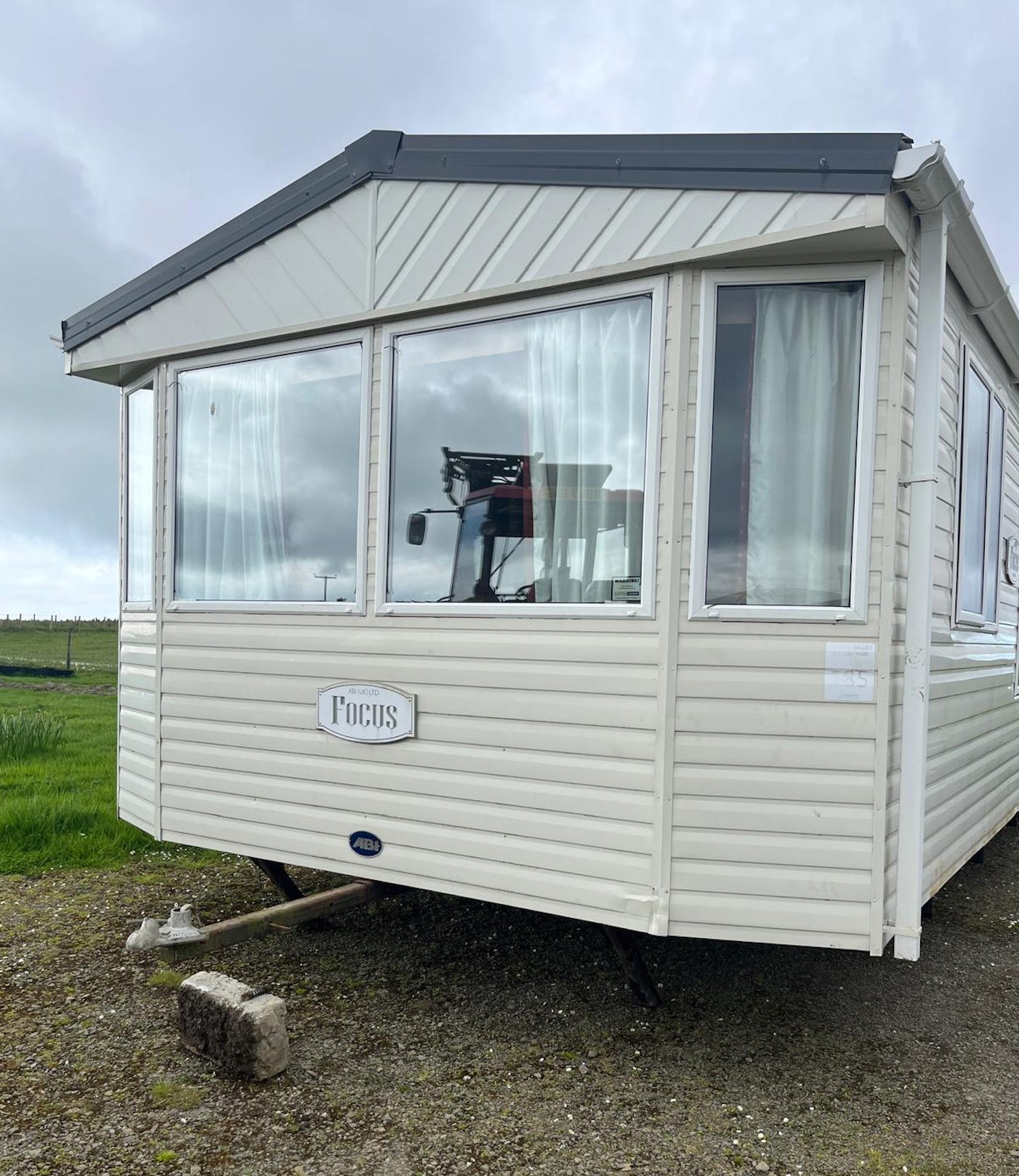 Image of a static caravan taken from the front. You can see the reflection of a tractor in the window