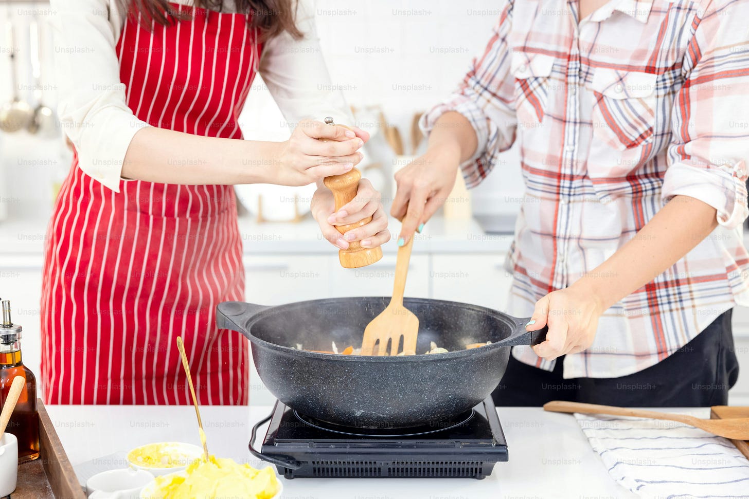 At home, two pals are having a good time in the kitchen. Sisters preparing spaghetti in the kitchen together. In the kitchen, two female pals