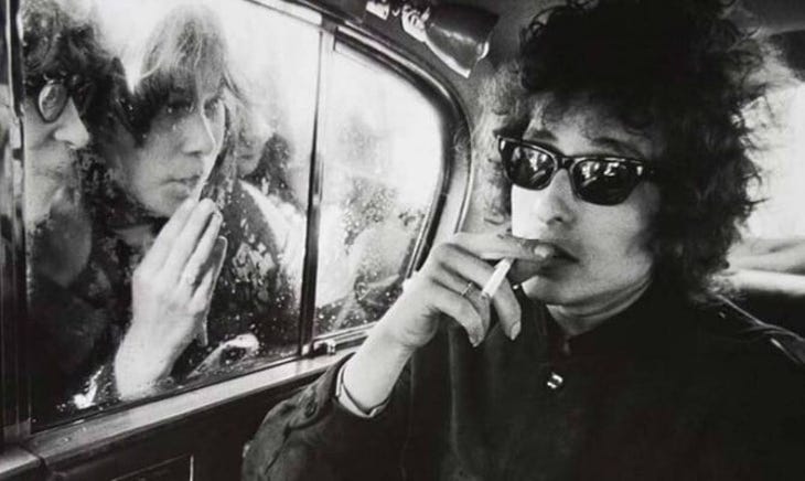 A black and white photo of Bob Dylan smoking in a car