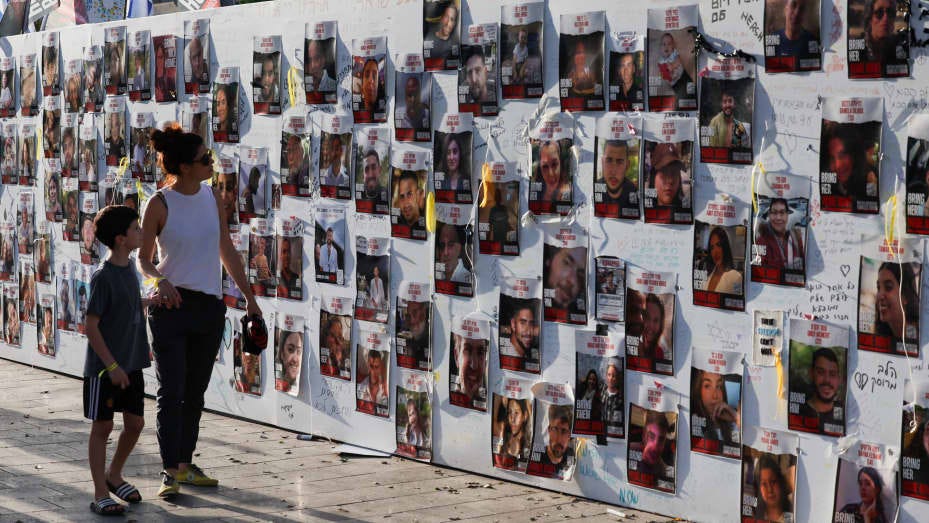 A woman with a child walks next to the wall with pictures, dedicated to hostages that are being held in Gaza after they were kidnapped from Israel by Hamas gunmen on October 7, as families and supporters of hostages hold a demonstration calling for their immediate release in Tel Aviv, Israel November 3, 2023. REUTERS/Ronen Zvulun