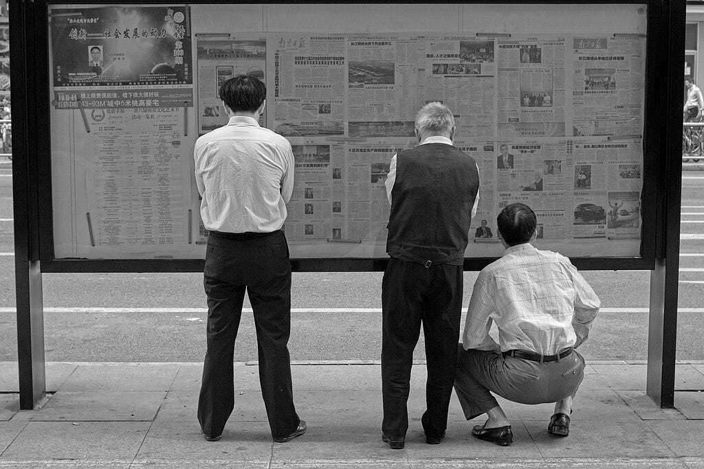 Black and white photo of three people reading newspapers.