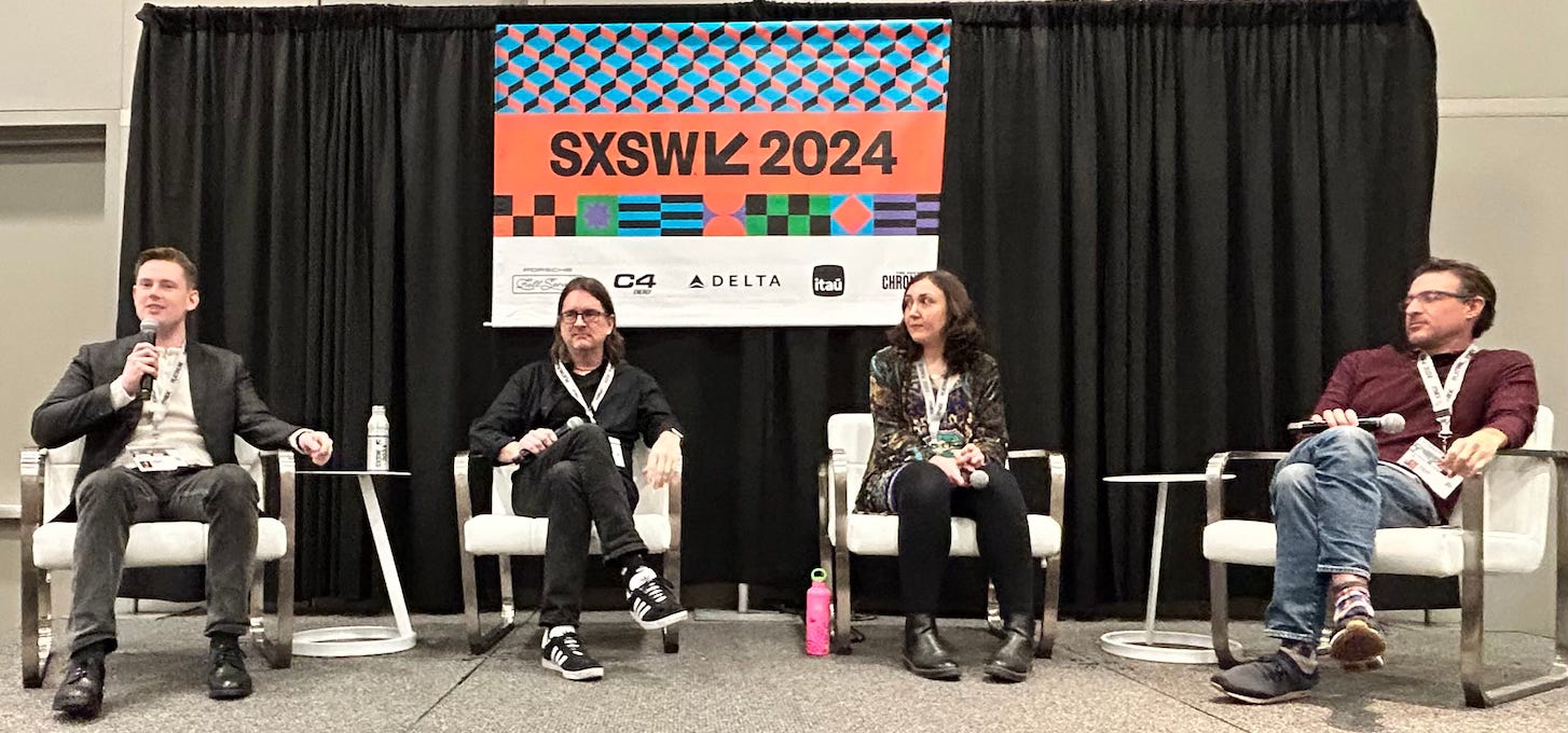 A photo of my panel at SXSW. The four panelists are seated on white chairs. A blue-orange SXSW sign hangs in back over a black curtain.