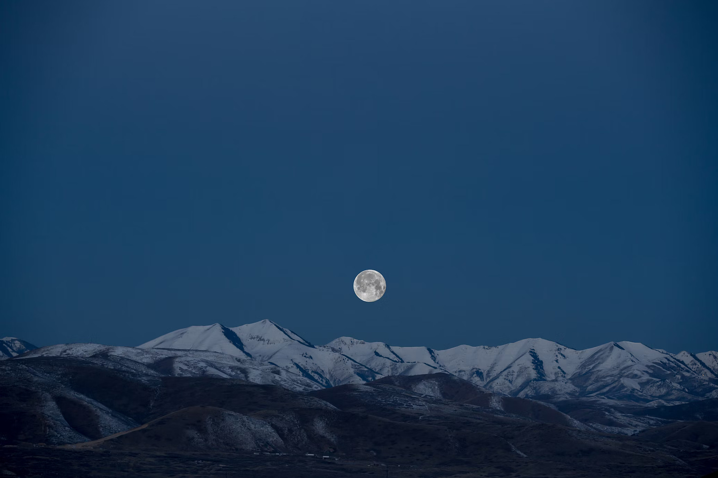 A full moon in a blue sky over  snowy mountains