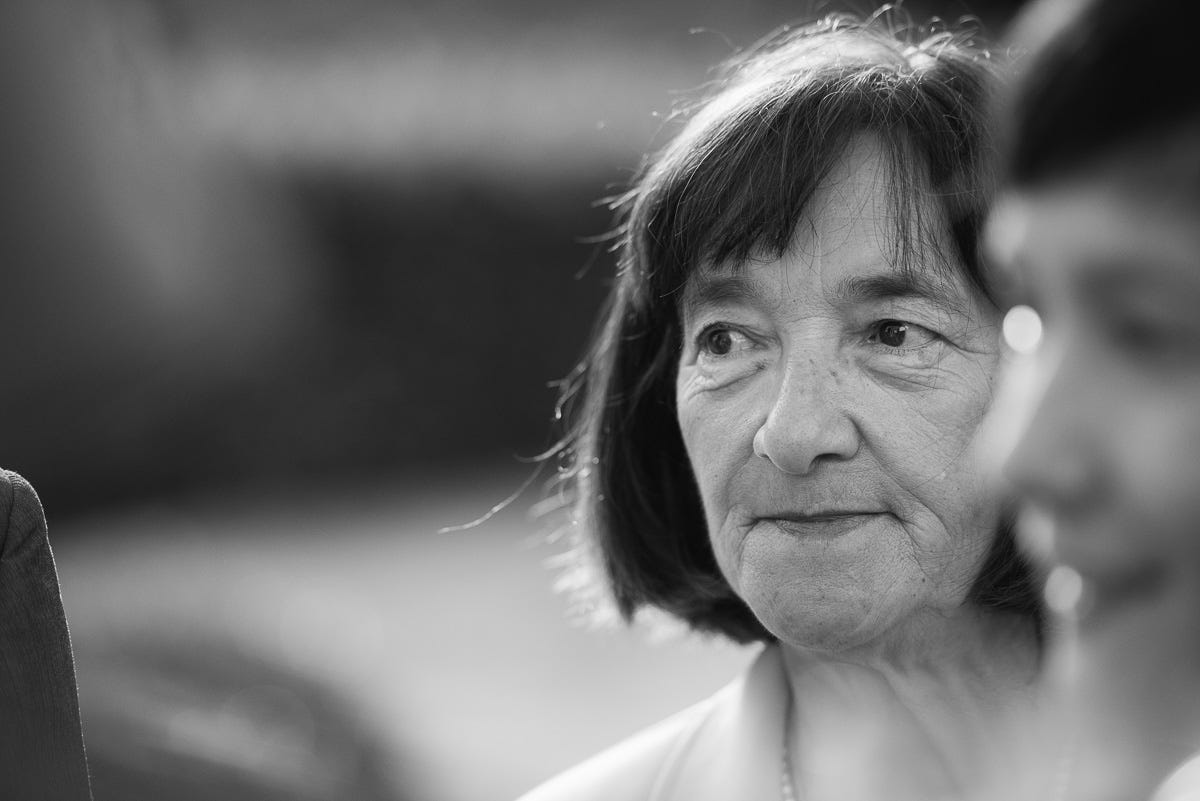 A black and white head shot of a 60 year old woman with a fringe and shouldeer lenght hair, gazing into the distance, empowered