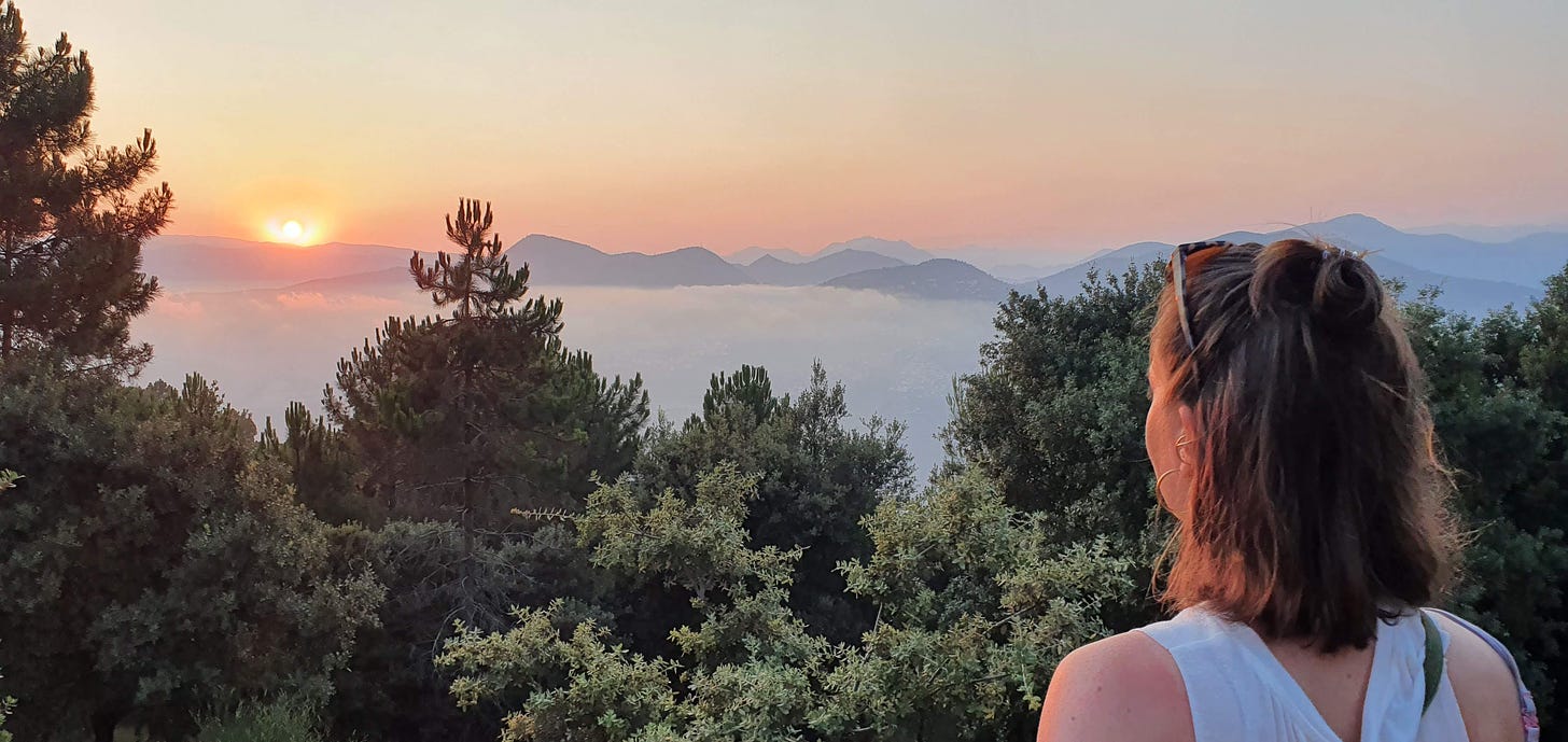 Anika Landsteiner schaut sich den Sonnenuntergang an. Im Hintergrund sind Berge sichtbar, im Tal steht Nebel