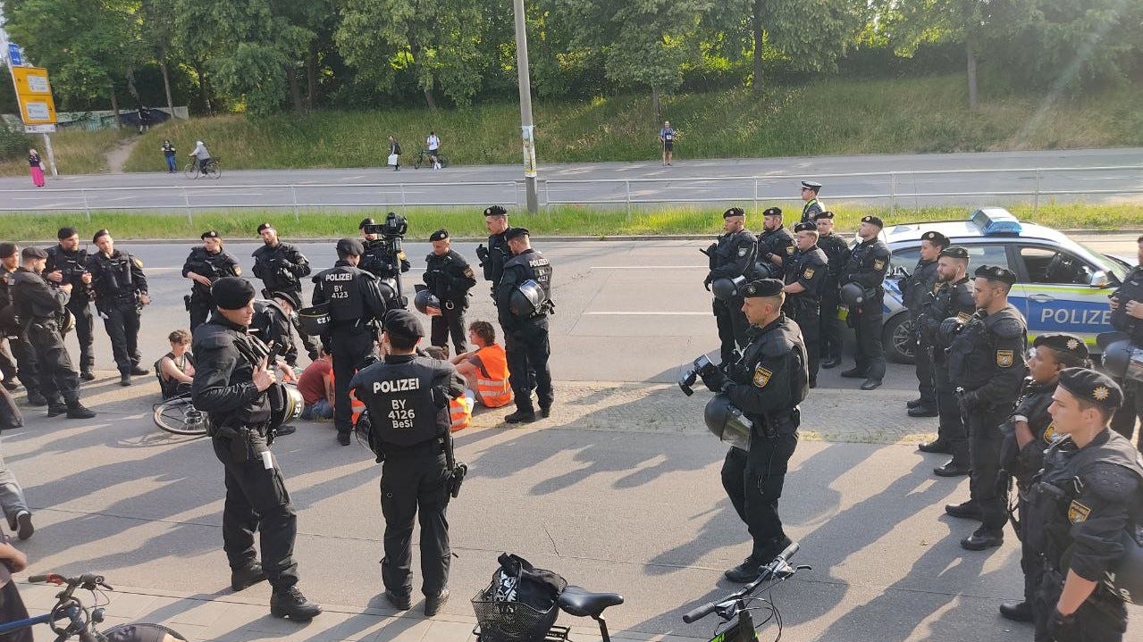 Eine große Gruppe schwarz gekleideter Polizisten, die um eine kleine Gruppe Demonstrierender stehen, welche am Boden sitzen.