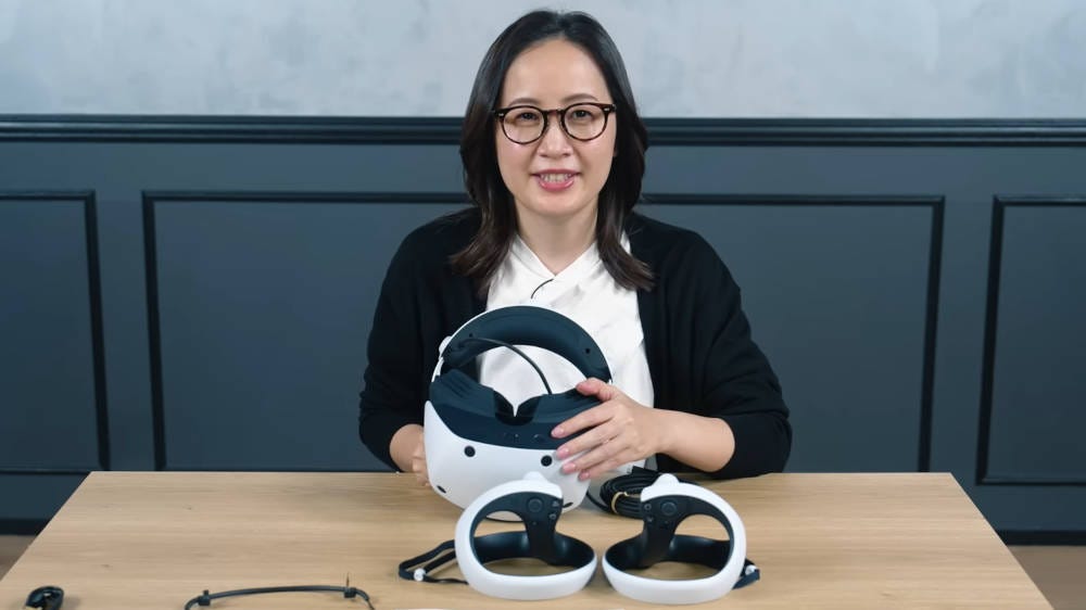 A woman wearing glasses and holding a PSVR 2 headset