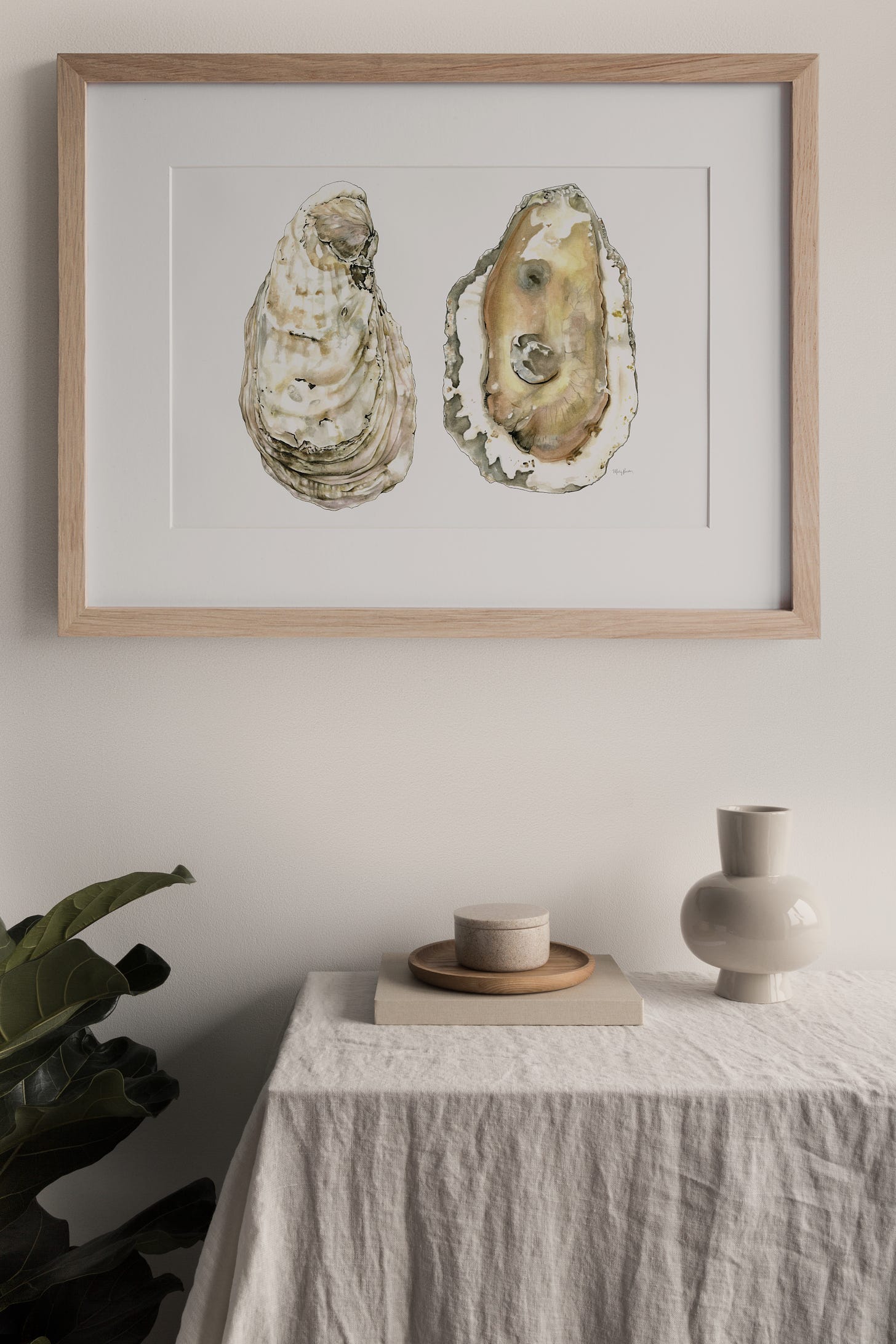 A photo of the oyster painting hanging in a frame above a table with a cloth and ceramics on it