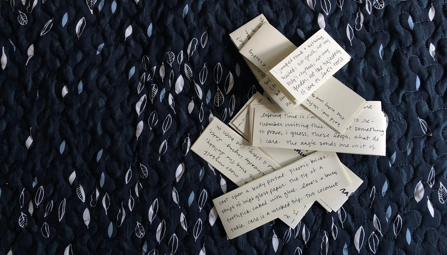 a pile of paper scraps, folded and written on in black ink, on a navy leaf-patterned bedspread