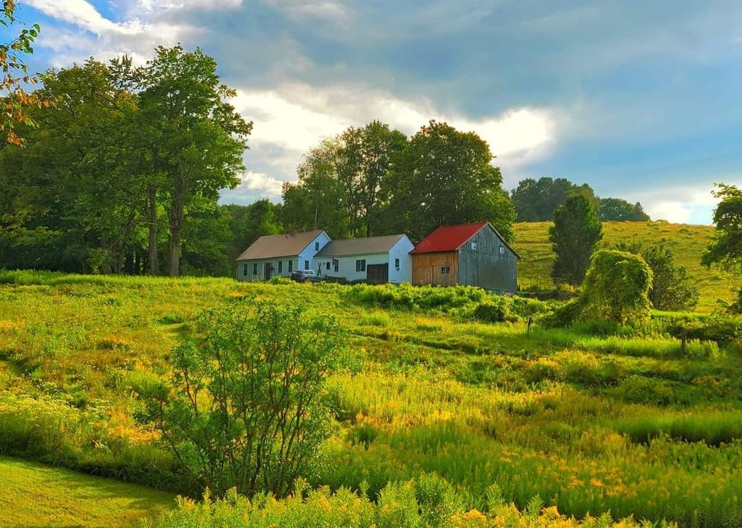 White Vermont farmhouse and barn with a red roof, set in green meadows and blue sky