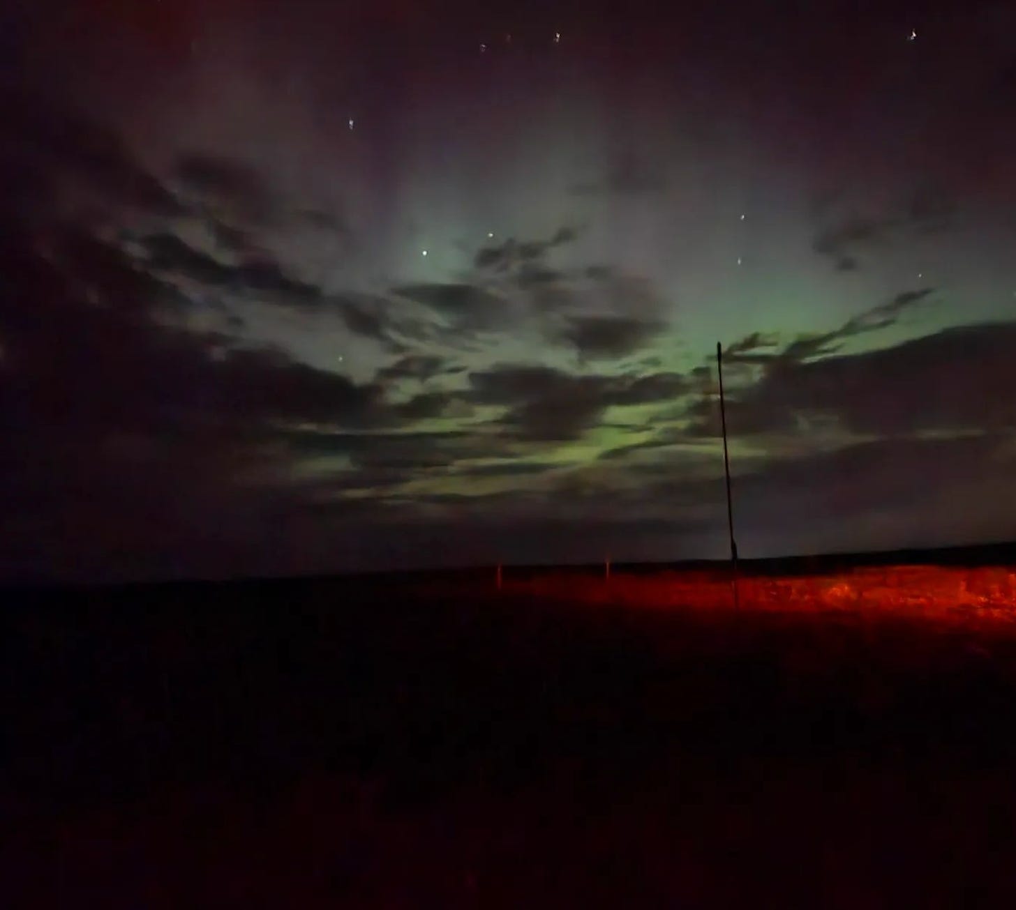 View of northern lights, faint, and blocked by clouds, over a field