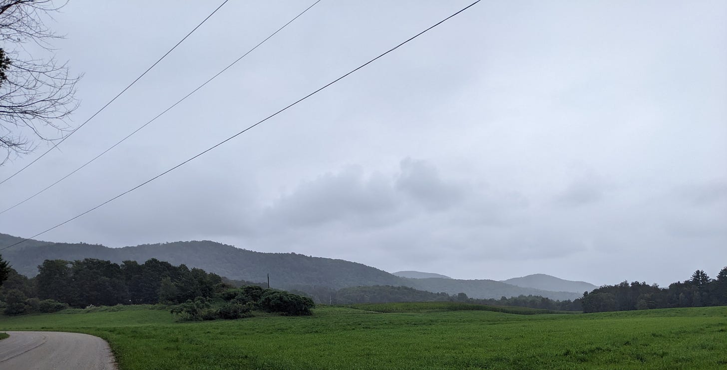 A view across a green field of low rolling mountains. the sky is gray and cloudy