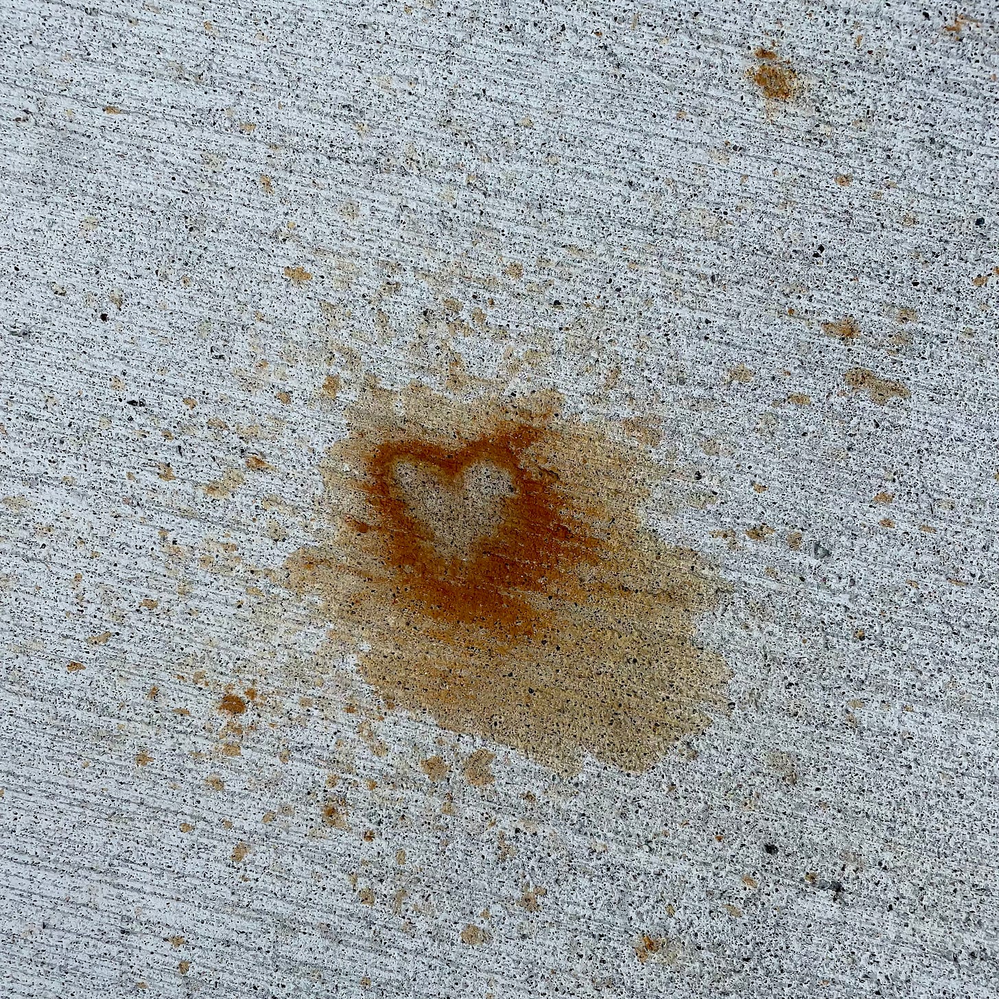 A close-up photo of a concrete surface with a rust-like stain in the center that resembles a heart shape.