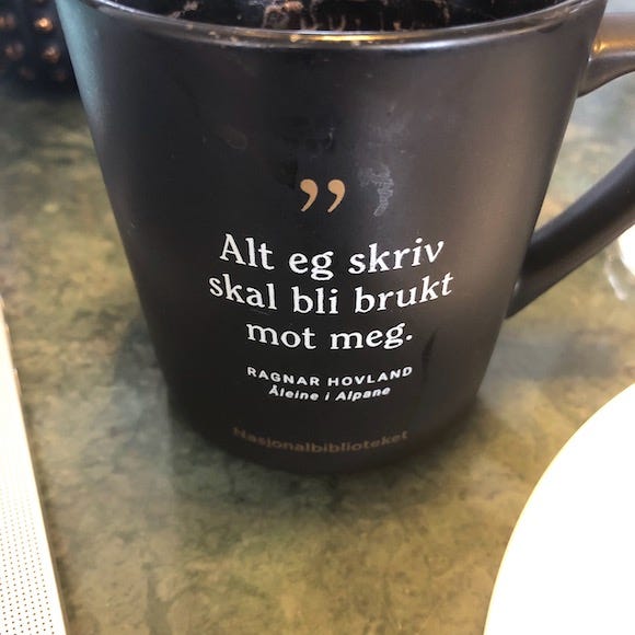 Svart kaffekopp med sitatet Alt eg skriv skal bli brukt mot meg av Ragnar Hovland.