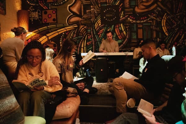 A Brooklyn bar is full of people, including a man behind a sound mixer, but instead of the usual scenes of drinking and laughing, patrons are reading. There’s a graphic mural along the back wall, and at least eight people engrossed in a book.