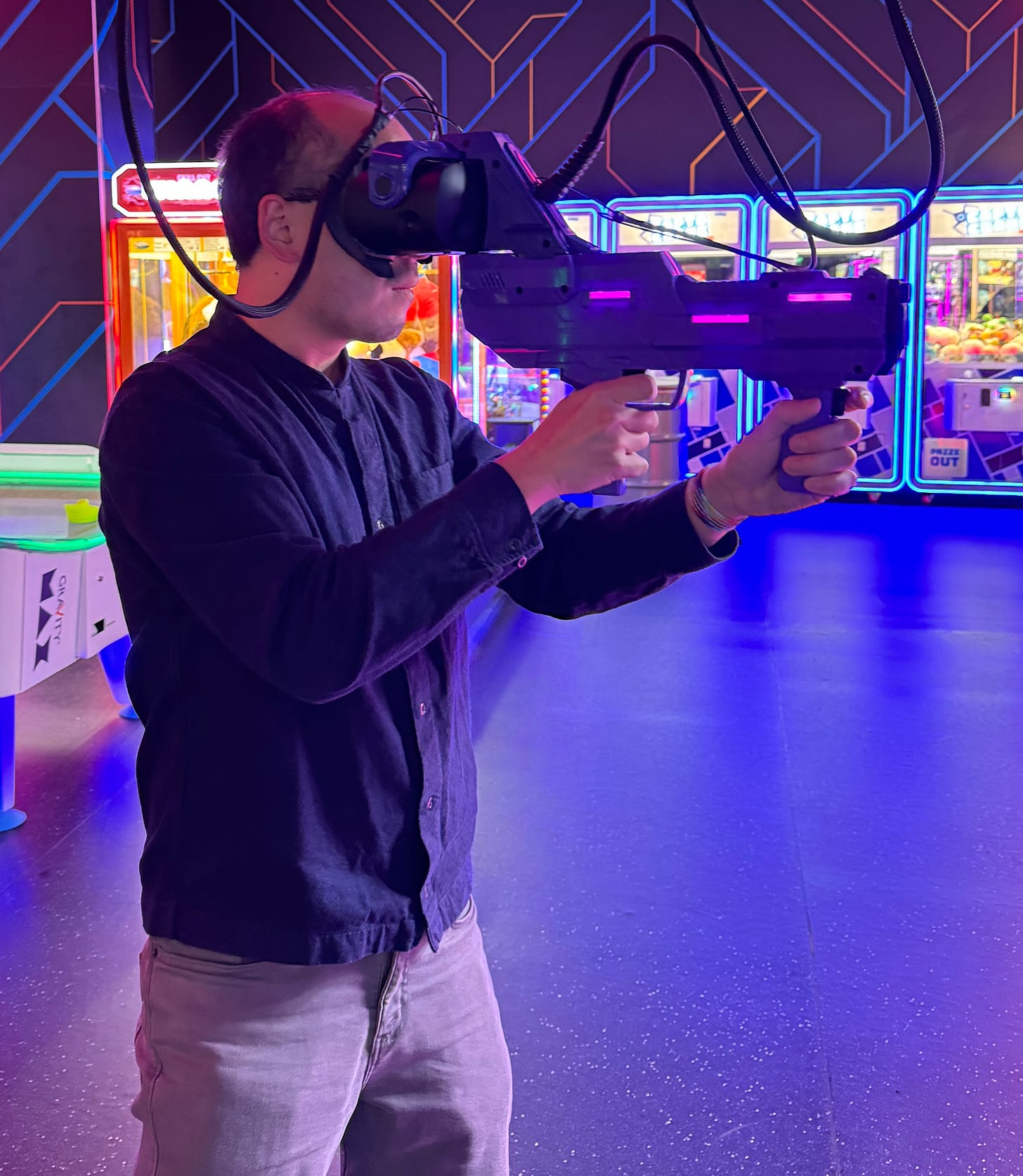 Adrian holds a gun with two hands, both fingers on triggers, with his face pressed against a VR headset embedded in the gun