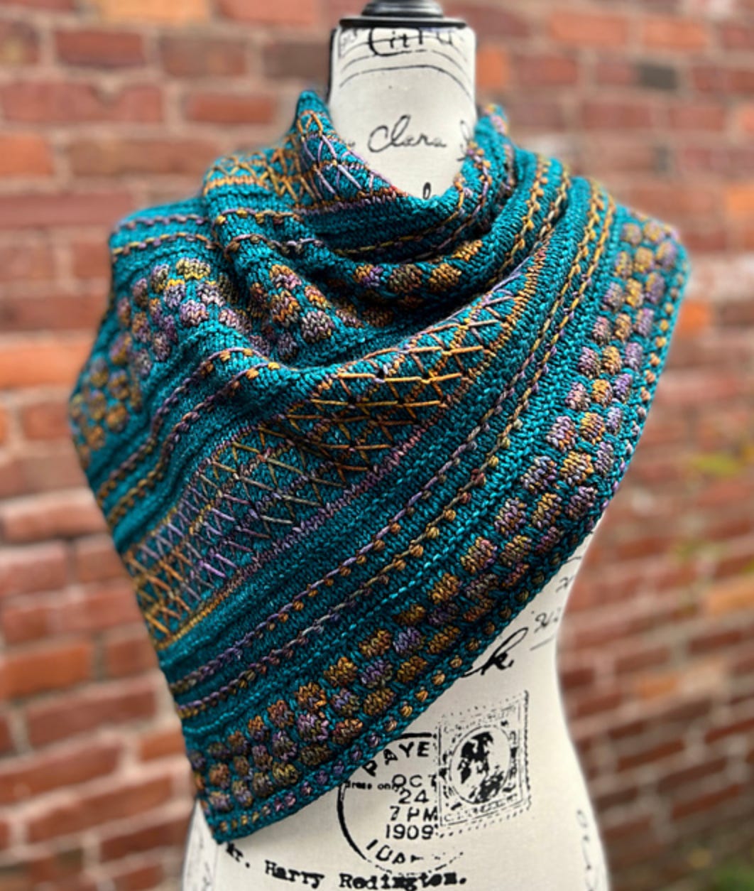 Killer Queen Cowl: A teal cowl with multicolored slip stitch work against a brick background