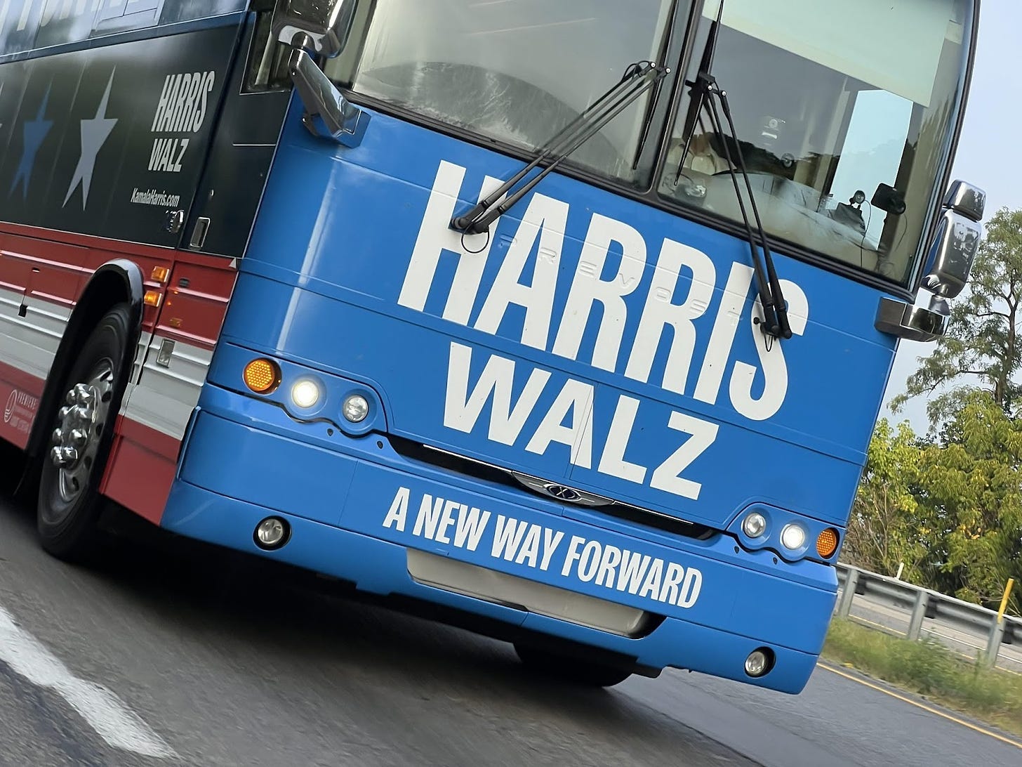 photo of the front of a Harris-Walz campaign bus on the road. text on the bus reads: Harris, Walz, A New Way Forward"