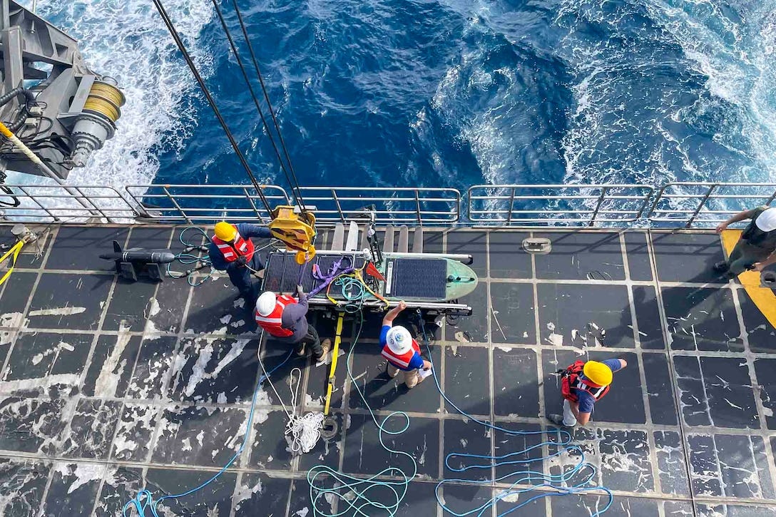 A look above sailors and other people working with equipment on the deck of a ship.