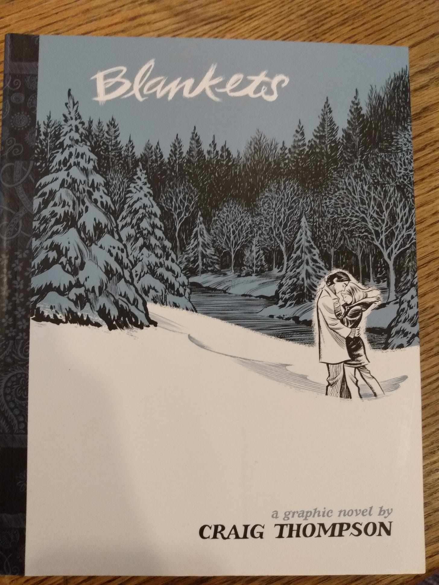 Portada de "Blankets", una novela gráfica de Craig Thompson. En la portada se ve a dos muchachos abrazados en medio de la nieve, con un fondo de bosque. 