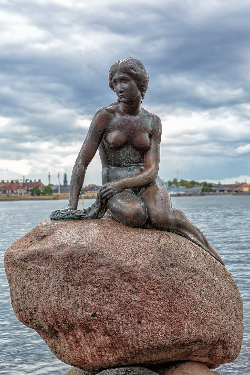 A statue of a mermaid sitting on a rock, surrounded by water.