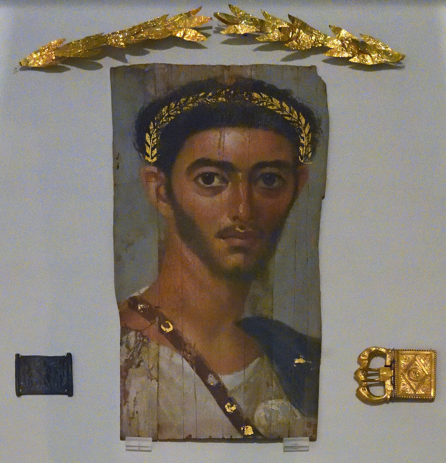 As a sign of his military service, the young officer from the time opf Emperor Hadrian wears a tunic, cloak and the gold-decorated sword belt, whereas the golden wreath in his hair could be connected with the cult of the dead. Sk 31161.2 Shown in the same display: Golden wreath and parts of a belt, 1st-3rd century AD.