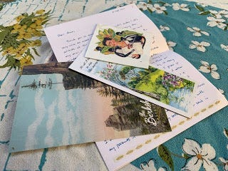 On a white and turquoise tablecloth, my first letter is laid out. It includes a postcard of mountains, a bookmark of green fields and a Frida Kahlo transfer.
