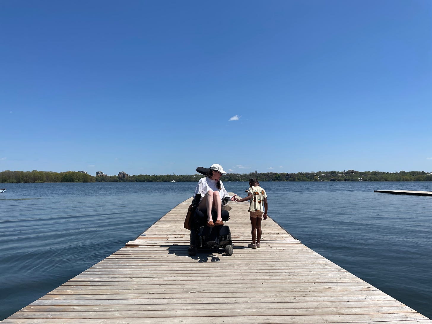 A white woman in a wheelchair holds hands with her black child on a dock