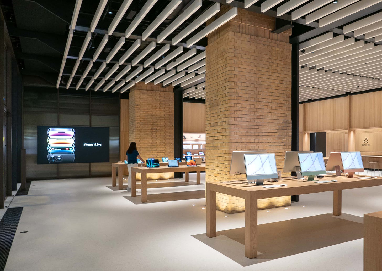 The interior of Apple Battersea at the front of the store. Large brick columns and white oak tables appear in the foreground.