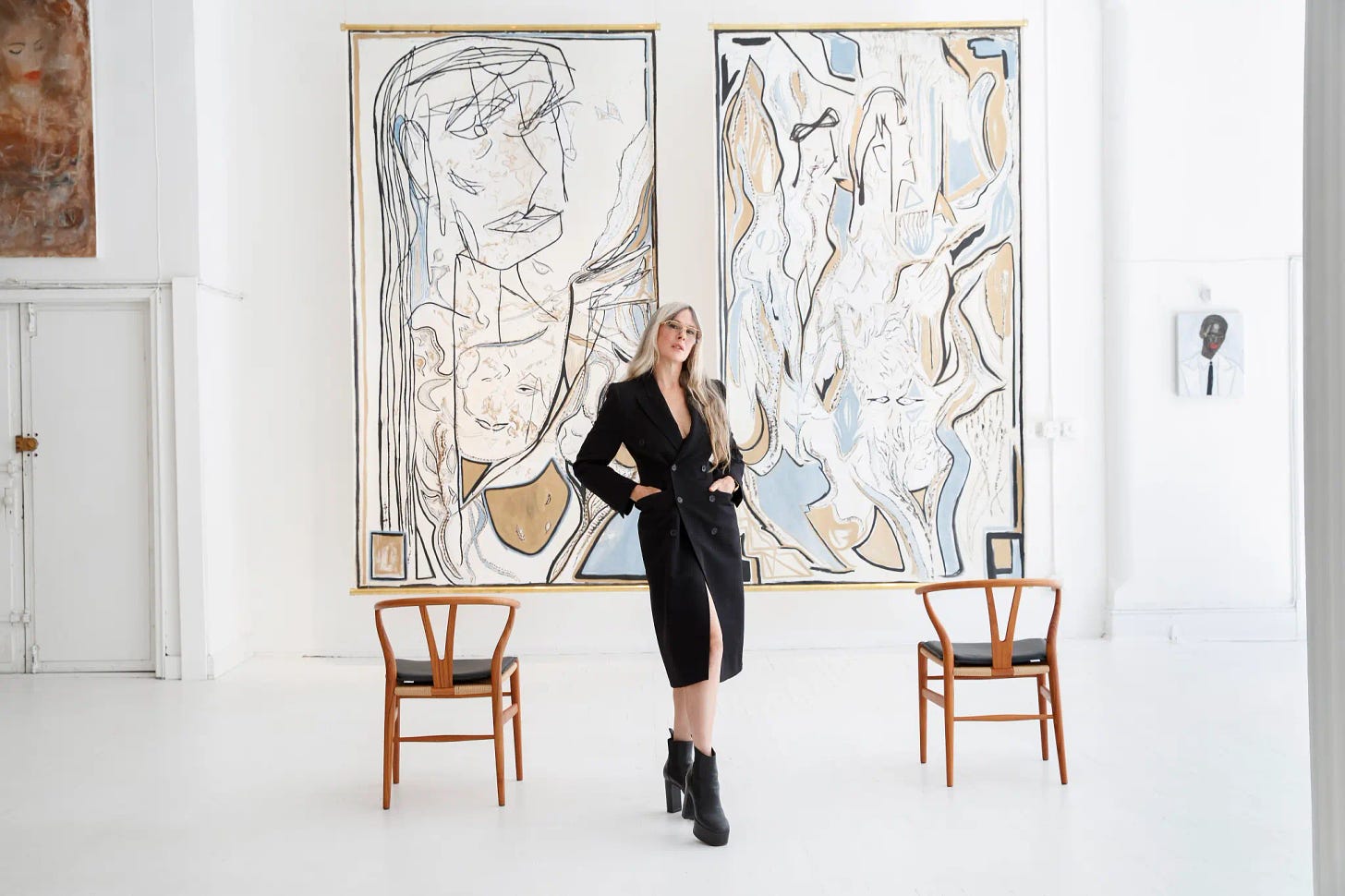 Fashion designer and painter Wendy Nichol stands in front of two of her abstract paintings featuring women's faces.